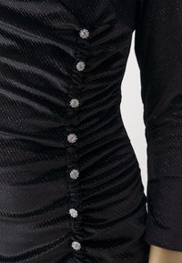 Tissu noir froncé avec une texture scintillante et une ligne verticale de huit boutons ronds argentés semblables à des pierres précieuses.