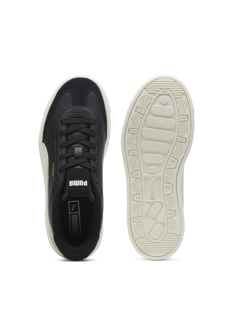 Baskets noires avec un dessus texturé, lacets à l'avant et une semelle en caoutchouc blanc présentant un motif de semelle géométrique. Détail du logo doré sur le côté.