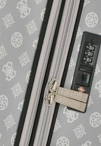 Valigia grigia con un motivo di loghi bianchi, doppie cerniere argento e una combinazione nera per la sicurezza.