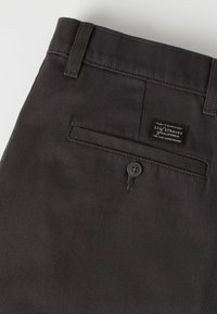 Κοντινό πλάνο σκούρου γκρι παντελονιού Levi Strauss που δείχνει πίσω τσέπη με κουμπί και ετικέτα της μάρκας πάνω από αυτή.