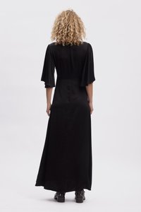 Black maxi dress with short flutter sleeves, smooth fabric, fitted bodice, and a flowing skirt, worn with ankle boots.