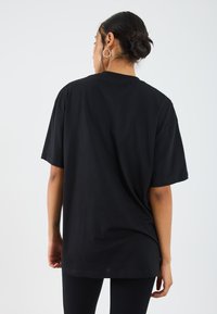 Black oversized t-shirt made of cotton, featuring short sleeves and a round neckline. Smooth texture with a relaxed fit design.