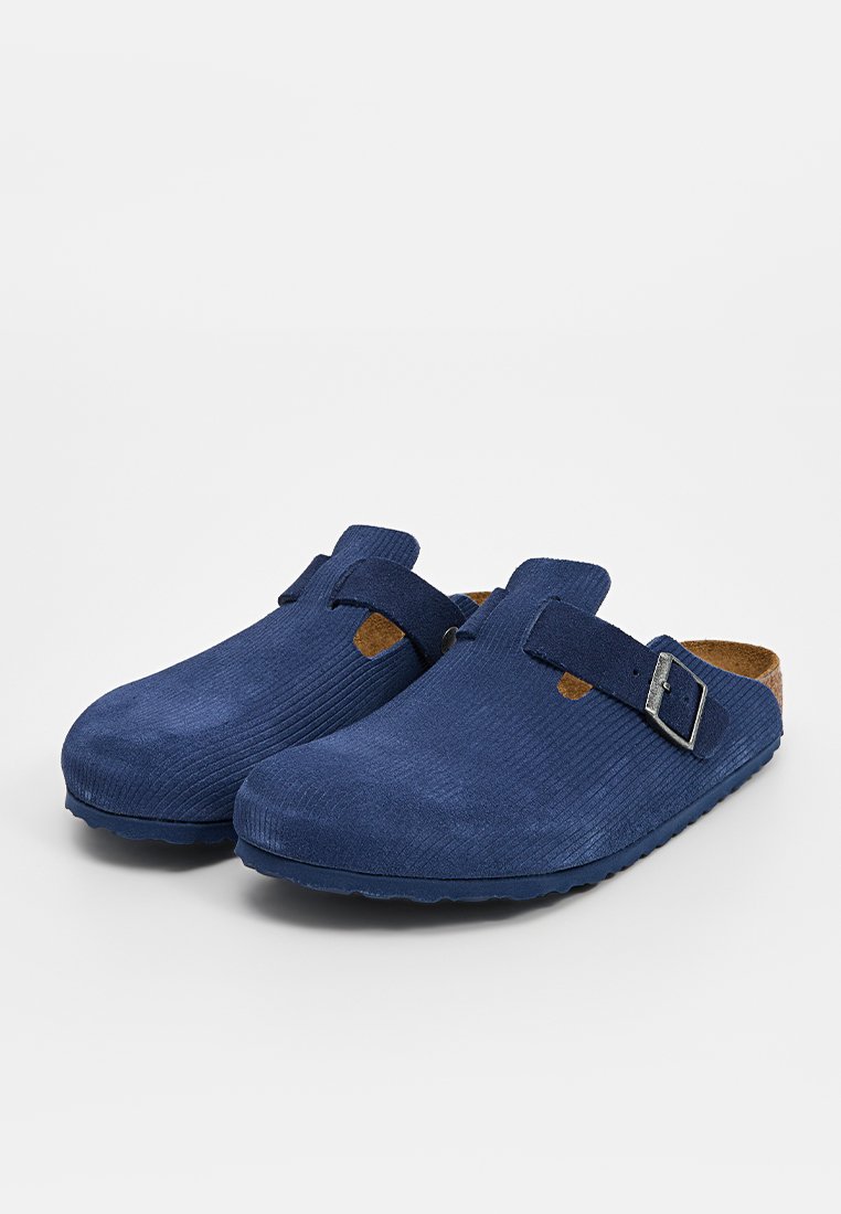 Blaue Clogs mit gerippter Textur, Korkfußbett und verstellbarem Riemen mit einer Metallschnalle. Leichte Konstruktion mit abgerundetem Zehenbereich.