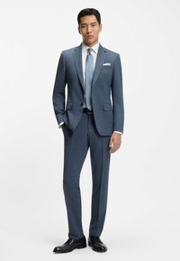 Blå mönstrad kostym med slim fit-design, kombinerad med en vit skjorta och ljusblå slips. Svarta finskor fulländar looken.