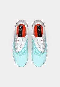 Ανοιχτό μπλε αθλητικά παπούτσια με λευκά κορδόνια, υφαντή επιφάνεια και ένα κοραλλί λογότυπο. Το εσωτερικό διαθέτει κόκκινη επένδυση και ετικέτα μάρκας.