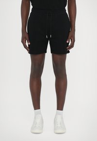 Sorte bomulds shorts med elastisk talje og snor. Enkel design, knælængde, parret med hvide sneakers og ankelsokker.
