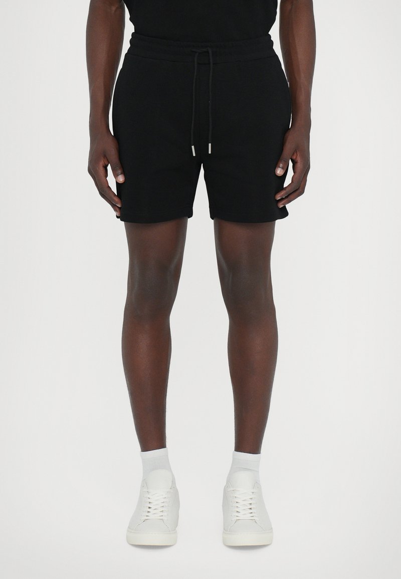 Sorte bomulds shorts med elastisk talje og snor. Enkel design, knælængde, parret med hvide sneakers og ankelsokker.