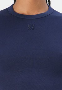 Navy blue ribbed T-shirt with a close-fitting round neckline and subtle embroidered "HUGO" logo at the chest. Soft, stretchy fabric.