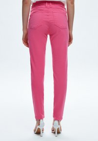 Rosa denimbyxor med smal passform, bakfickor och en mjuk textur, tillsammans med vita högklackade sandaler.