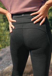Léggings noirs taille haute en tissu texturé, avec des accents brodés et un petit logo au niveau de la taille. Design ajusté.