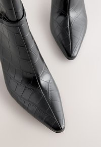Black pointed-toe ankle boots with crocodile embossed leather texture on a light background.