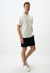 T-shirt blanche à manches courtes avec un col rond, associée à un short noir et des baskets blanches. Texture lisse et design simple et moderne.