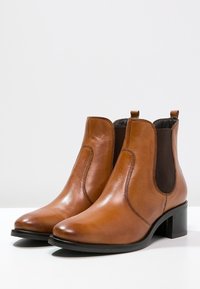 Stivali alla caviglia in pelle marrone con pannelli elastici laterali, punta arrotondata, texture liscia e tacco basso a blocco. Design tipico delle Chelsea boots.