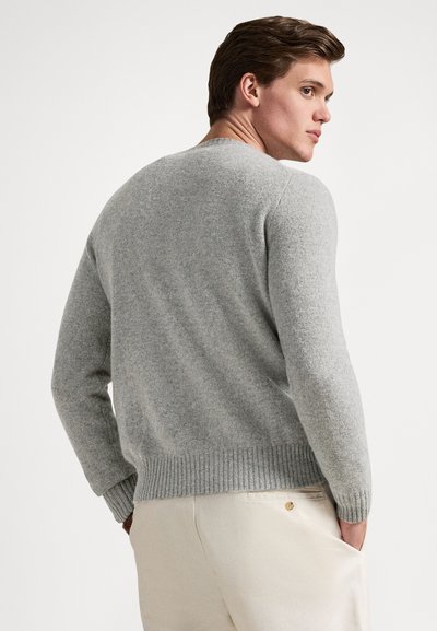 Γκρι πλεκτό πουλόβερ με ριμπ τελείωμα και μανσέτες. Απλή σχεδίαση με στρογγυλή λαιμόκοψη, εμφανίζεται από πίσω, συνδυασμένο με ανοιχτόχρωμο παντελόνι.