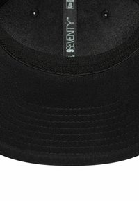 Cappellino snapback nero con visiera piatta, realizzato in tessuto testurizzato, con cucitura a vista e occhielli di ventilazione. Etichetta interna visibile.