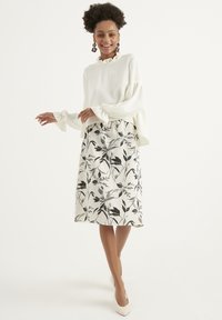 Maglione bianco a coste con polsini arricciati abbinato a una gonna fino al ginocchio con stampa floreale nera su sfondo chiaro.
