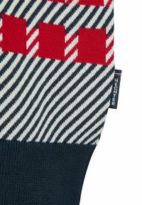 Strickpullover mit rot-weißer Schachbrettmuster über einem navy blauen Rippenbund, mit diagonalen schwarz-weißen Streifen dazwischen.