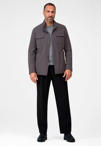 Gray, lightweight jacket with a high collar, front pockets, and a zip closure, paired with black pants and black shoes. Clean, modern design.