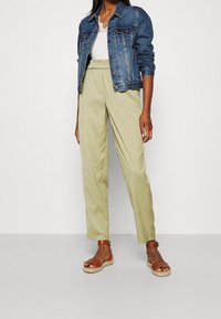 Chaqueta vaquera, pantalones verdes claros con cintura elástica y sandalias marrones de tiras. Tela suave, ajuste relajado y diseño informal.