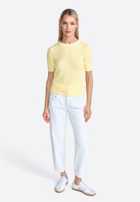 Maglione giallo a maniche corte in maglia con una finitura testurizzata, abbinato a pantaloni bianchi a vestibilità rilassata e sneakers bianche con suola beige.