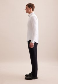 Biała koszula z długim rękawem i spiczastym kołnierzykiem, połączona z czarnymi spodniami i czarnymi sznurowanymi butami. Gładki materiał, dopasowany krój.