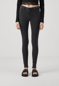 Høyt liv svarte smale jeans med en jevn denimtekstur, frontlommer og synlig søm. Kombinert med svarte brede sandaler.