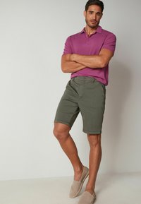 Lila kortärmad polo, olivgröna shorts och beige slip-on skor. Shorts har en skräddarsydd design med rullade fållar.