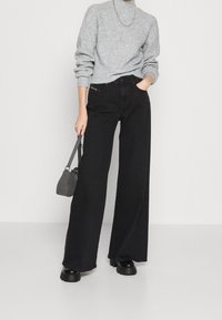 Jean noir à jambes larges avec une taille haute et des poches avant, associé à un pull gris. Les accessoires comprennent un petit sac gris et des chaussures noires.