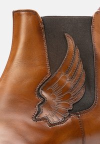 Brown leather ankle boot with elastic panels and a decorative wing design. Smooth texture, sturdy stitching, and contrasting black elastic.