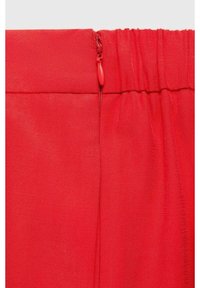 Tejido rojo con una textura suave, con un cierre con cremallera visible en la cintura. El diseño incluye detalles de elastano fruncido.
