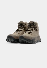 Beżowe buty trekkingowe z teksturowanymi gumowymi podeszwami, wzmocnionymi czubkami i czarno-pomarańczowymi sznurówkami. Średni model zapewniający wsparcie dla kostek.