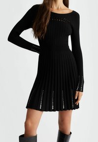 Robe noire à côtes avec manches longues, dotée d'un décolleté carré, de découpes décoratives et de clous en argent le long de l'ourlet et des poignets.