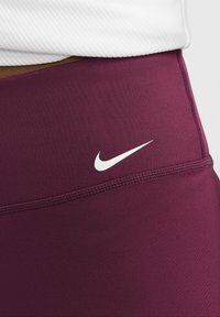 Bordeaux sportlegging gemaakt van rekbaar materiaal, met een contrasterend wit Nike swoosh-logo en flatlock-stitchedetails.