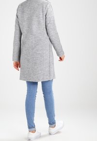Abrigo de mezcla de lana gris con un corte recto, detalles de costura y un cuello alto, combinado con jeans azul claro y zapatillas blancas.
