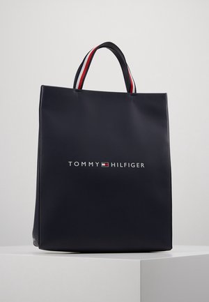 Sac cabas bleu foncé Tommy Hilfiger avec des anses courtes, présentant des rayures rouges, blanches et bleues ainsi que le logo de la marque centré à l'avant.