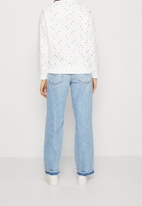 Felpa bianca con motivi a pois colorati, abbinata a jeans a gamba larga blu chiaro con orlo sfilacciato e sneakers bianche.