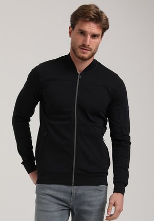 Zwarte ritssluitingenjacket met een hoge kraag, lange mouwen, voorzakken en een strakke uitstraling. Gemaakt van een zachte, rekbare stof.