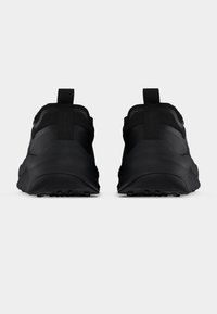 Ζευγάρι μαύρα αθλητικά παπούτσια, ορατά από πίσω, με ταινίες έλξης και χοντρές, υφασμένες σόλες σε μονόχρωμο φόντο.