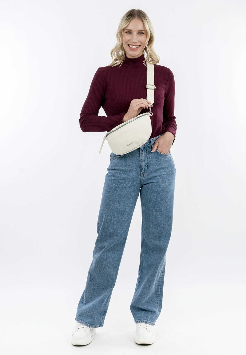 Sac en bandoulière beige avec une finition texturée et une fermeture éclair, porté par une personne vêtue d'un haut ajusté bordeaux et d'un jean taille haute bleu.