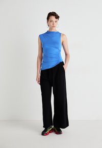 Top albastru, fără mâneci, cu detalii din material pliat pe lateral; asortat cu pantaloni negri, largi și adidași negri cu accente strălucitoare.