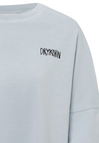 Lichtblauwe katoenen sweatshirt met geribde ronde hals en zwart geborduurd "DRYKORN" logo op de linkerborst.