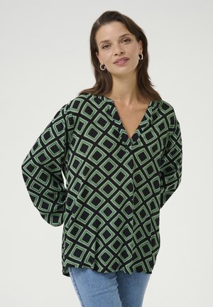 Blouse à motifs verts et noirs avec un col en V, des manches longues et une coupe ample, arborant un design géométrique en diamant.