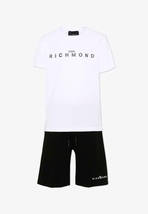 T-shirt blanc à manches courtes avec le texte « John Richmond » et short noir à cordon de serrage avec un petit texte assorti sur une jambe.