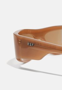 Bruine doorzichtige zonnebril met een slank ontwerp. Heeft een lichte kromming en een klein "RSF"-logo in zilver op de poot. Gladde textuur.