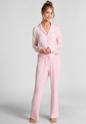 Lichtroze pyjama-set met een lange mouwen knoop blouse met een borstzak, en een broek met elastische trekkoord in de taille. Zachte stoftextuur.