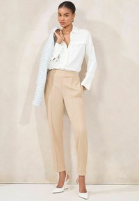Crème blouse met een kraag, beige pantalon met elastische tailleband, en witte slingbackhakken, gestyled met een lichtblauwe geweven jas.
