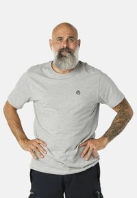Szürke anyagú pamut póló, kerek nyakkivágással és rövid ujjakkal; a bal mellrészen egy kis fekete logó található; sima tapintású.