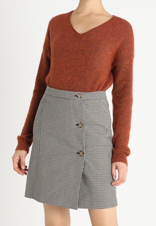 Pull à col en V de couleur rouille, en tissu duveteux, associé à une jupe à carreaux noir et blanc avec des boutons à l'avant et une silhouette évasée.