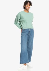 Felpa trapuntata verde menta con vestibilità rilassata, abbinata a jeans a gamba larga azzurri con vita alta e sneakers bianche.