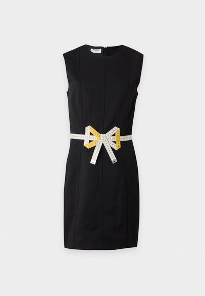 Robe noire sans manches longueur genoux avec taille cintrée et nœud fait de ruban à mesurer jaune et blanc autour de la taille.